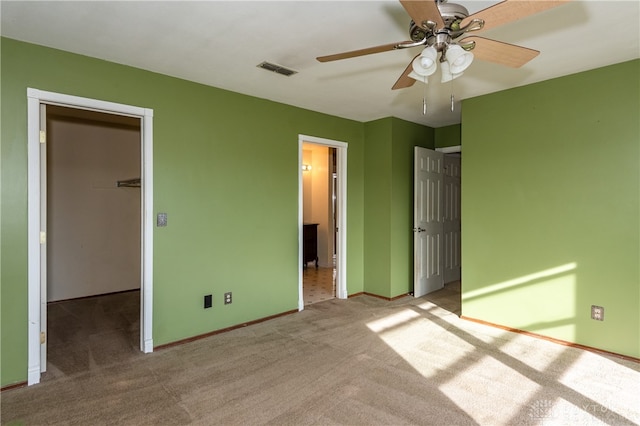 unfurnished bedroom featuring light carpet, a walk in closet, a closet, and ceiling fan