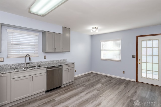 kitchen with light stone counters, light hardwood / wood-style flooring, dishwasher, gray cabinetry, and sink