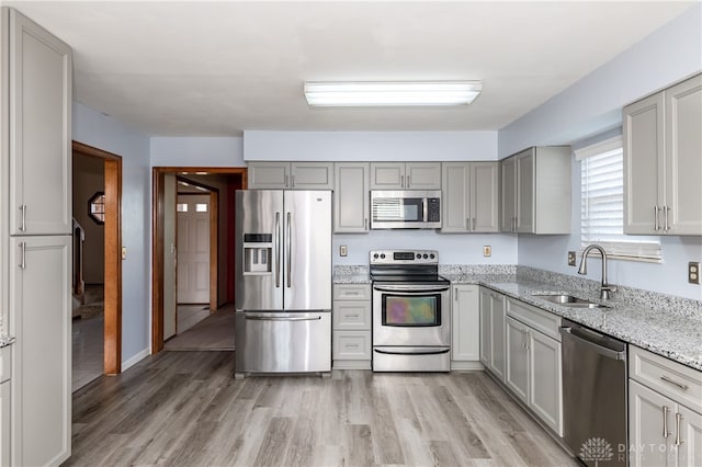 kitchen with light stone countertops, light wood-type flooring, sink, gray cabinetry, and stainless steel appliances