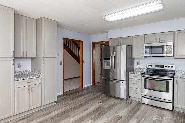 kitchen featuring gray cabinets, appliances with stainless steel finishes, light stone counters, and light wood-type flooring