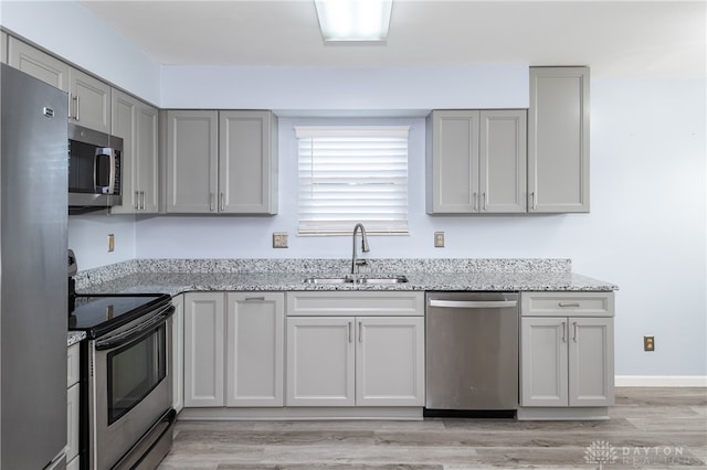 kitchen with light stone countertops, appliances with stainless steel finishes, sink, light hardwood / wood-style floors, and gray cabinets