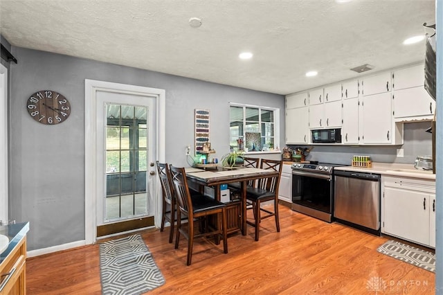 kitchen featuring sink, stainless steel appliances, a textured ceiling, white cabinets, and light wood-type flooring