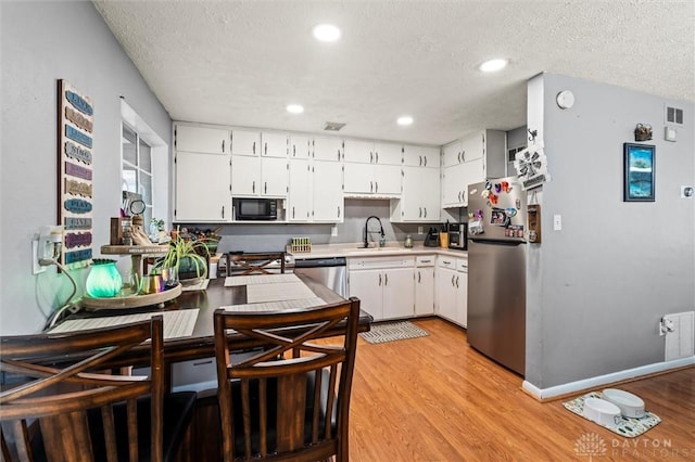 kitchen with sink, a textured ceiling, appliances with stainless steel finishes, light hardwood / wood-style floors, and white cabinetry