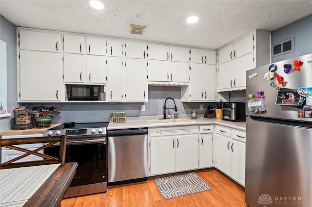 kitchen featuring white cabinets, sink, light hardwood / wood-style flooring, a textured ceiling, and appliances with stainless steel finishes