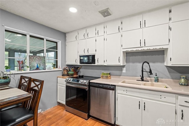 kitchen featuring appliances with stainless steel finishes, light hardwood / wood-style floors, white cabinetry, and sink