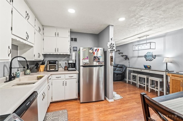 kitchen with sink, appliances with stainless steel finishes, a textured ceiling, white cabinets, and light wood-type flooring