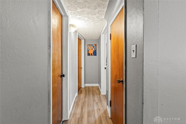 hall with a textured ceiling and light wood-type flooring