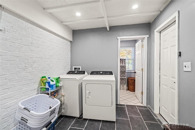 laundry room featuring washer and clothes dryer, brick wall, and dark tile patterned flooring