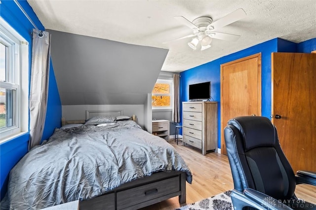 bedroom featuring a textured ceiling, ceiling fan, light hardwood / wood-style floors, and vaulted ceiling