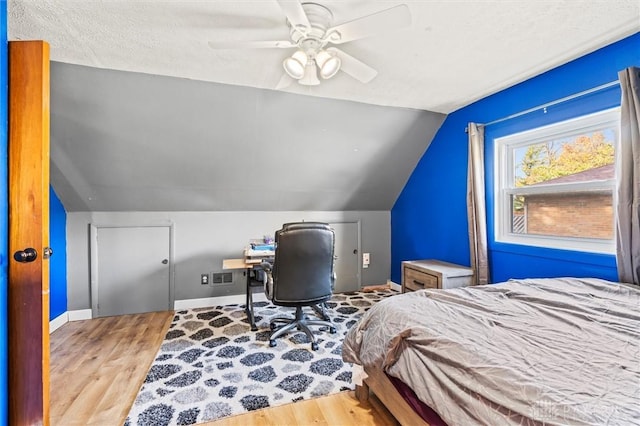 bedroom with ceiling fan, lofted ceiling, a textured ceiling, and light hardwood / wood-style flooring