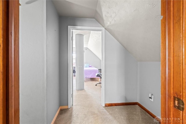 hallway with light colored carpet and lofted ceiling