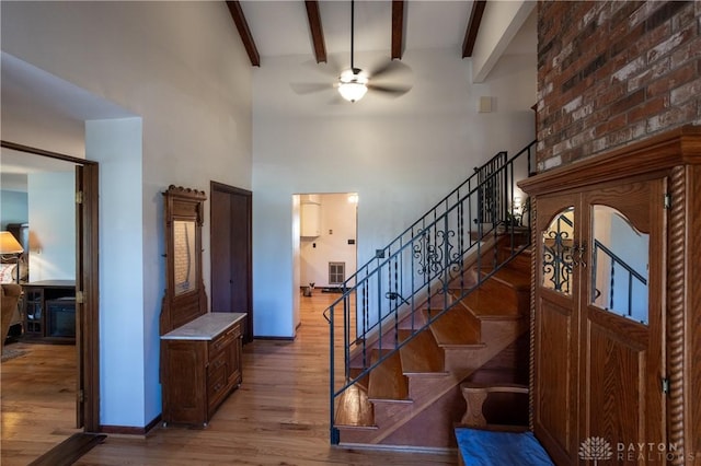 stairs with a towering ceiling, ceiling fan, hardwood / wood-style floors, and beamed ceiling