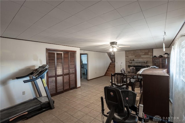 exercise room with a stone fireplace and ceiling fan