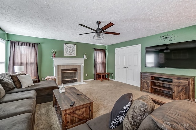 carpeted living room with a textured ceiling, ceiling fan, and a tiled fireplace