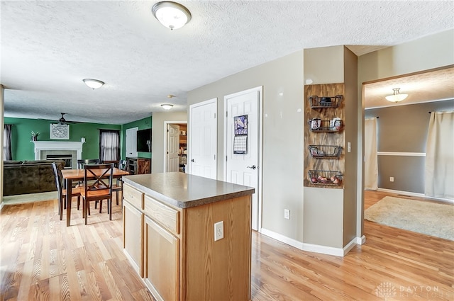 kitchen with ceiling fan, a kitchen island, light hardwood / wood-style floors, and a textured ceiling