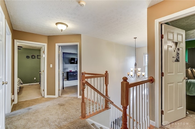 corridor featuring light carpet, a textured ceiling, and a notable chandelier