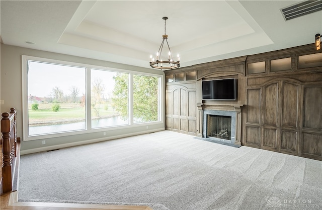 unfurnished living room with light carpet, a notable chandelier, a fireplace, and a raised ceiling