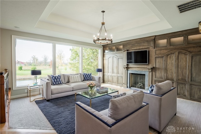 living room with a tray ceiling, a chandelier, and a high end fireplace