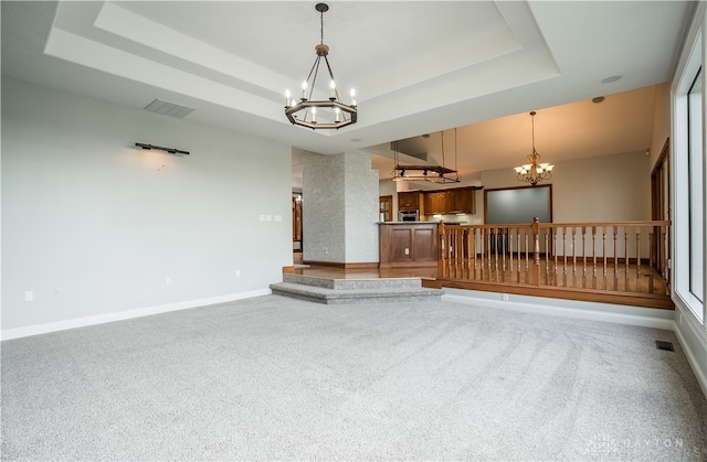 unfurnished living room featuring carpet flooring, a tray ceiling, and an inviting chandelier