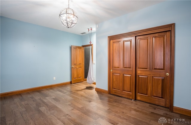 unfurnished bedroom featuring a chandelier and wood-type flooring