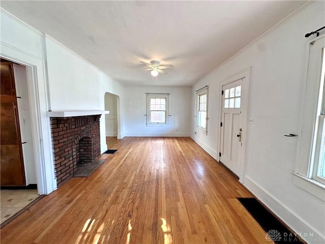 unfurnished living room with ceiling fan, ornamental molding, light hardwood / wood-style floors, and a brick fireplace