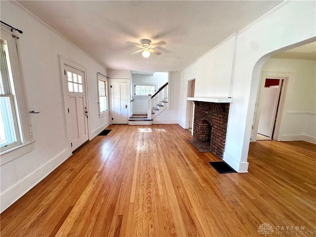 unfurnished living room featuring ceiling fan, a fireplace, ornamental molding, and light hardwood / wood-style flooring