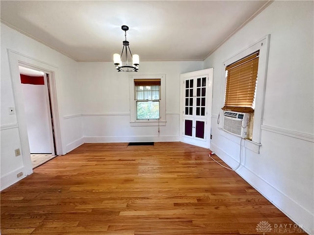 unfurnished dining area with hardwood / wood-style floors, cooling unit, ornamental molding, and an inviting chandelier