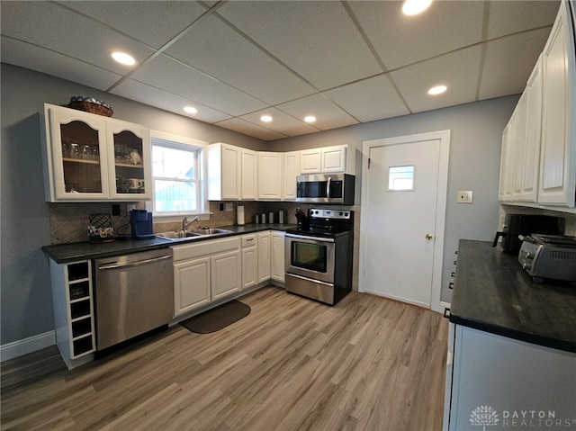 kitchen featuring white cabinets, tasteful backsplash, appliances with stainless steel finishes, a paneled ceiling, and light hardwood / wood-style flooring