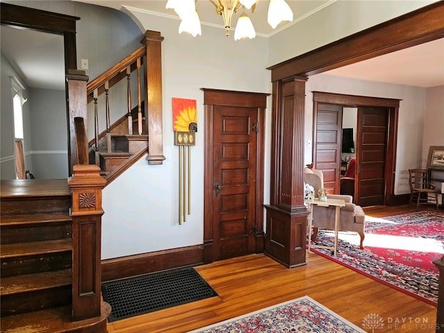 entryway featuring crown molding, hardwood / wood-style flooring, decorative columns, and a chandelier