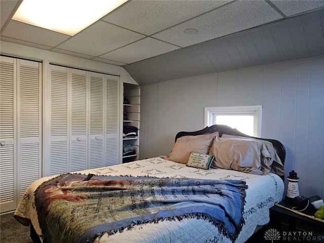 bedroom with a paneled ceiling, carpet floors, and two closets