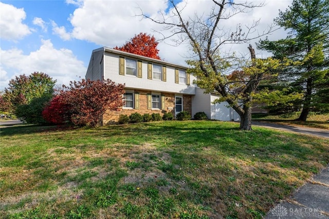 colonial-style house with brick siding, a front yard, aphalt driveway, and a garage