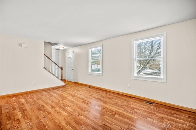 unfurnished living room featuring baseboards, light wood-style floors, visible vents, and stairway