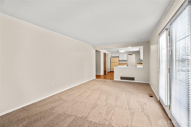 unfurnished living room with baseboards, visible vents, and light carpet