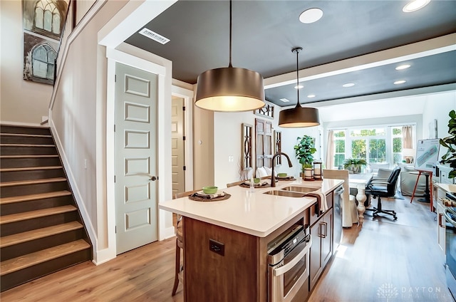 kitchen featuring pendant lighting, a center island with sink, sink, light wood-type flooring, and appliances with stainless steel finishes