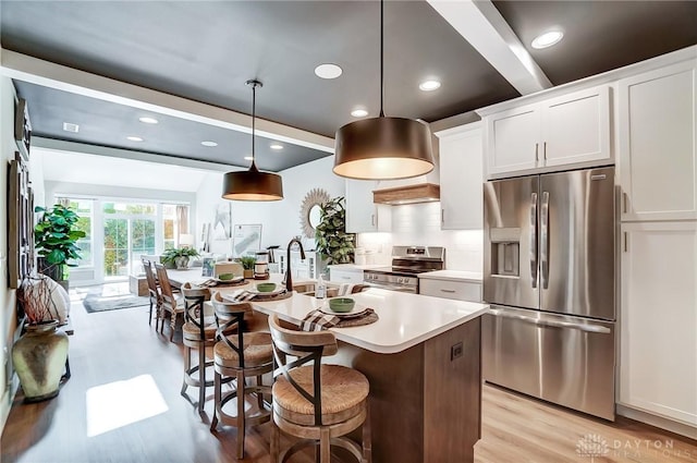 kitchen featuring decorative light fixtures, a kitchen island with sink, a breakfast bar, white cabinets, and appliances with stainless steel finishes