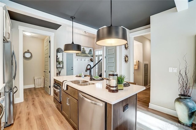 kitchen with stainless steel appliances, sink, a center island with sink, light hardwood / wood-style floors, and hanging light fixtures