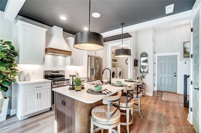 kitchen with pendant lighting, premium range hood, washer and dryer, appliances with stainless steel finishes, and white cabinetry