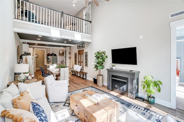 living room with hardwood / wood-style flooring, ceiling fan, a towering ceiling, and a fireplace