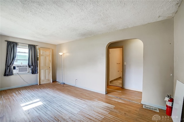 empty room with light hardwood / wood-style flooring, a textured ceiling, and cooling unit