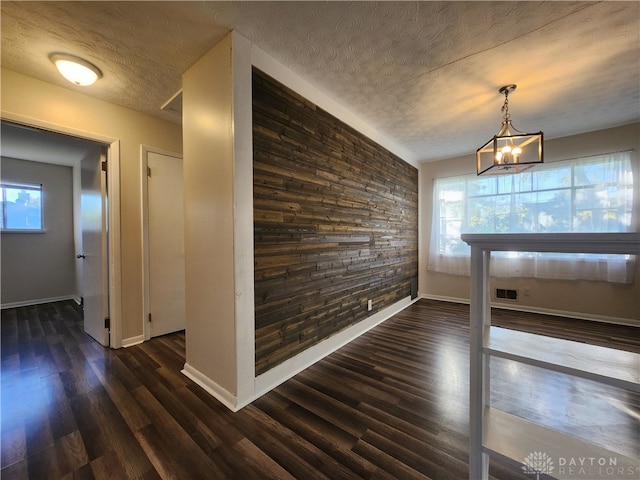 unfurnished dining area featuring a textured ceiling, an inviting chandelier, and dark hardwood / wood-style flooring