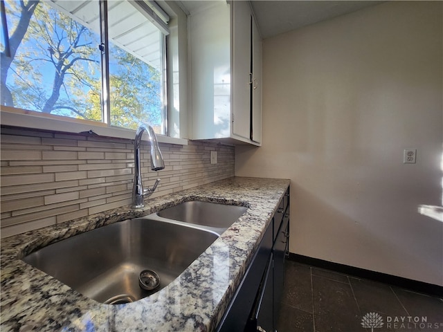 kitchen with tasteful backsplash, sink, dark tile patterned floors, white cabinets, and light stone counters