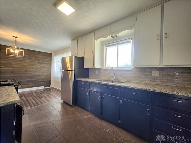 kitchen with wooden walls, stainless steel appliances, decorative light fixtures, blue cabinetry, and white cabinetry