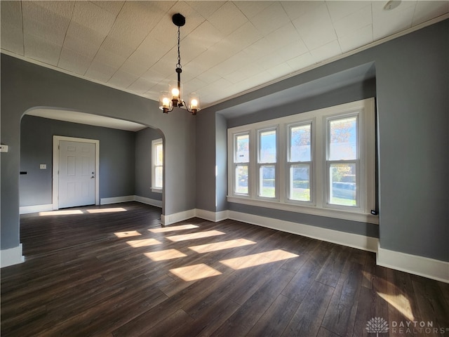 spare room featuring dark wood-type flooring, a notable chandelier, and a healthy amount of sunlight