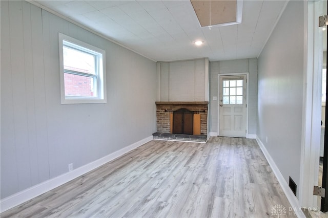 unfurnished living room with wooden walls, a wealth of natural light, light wood-type flooring, and a brick fireplace