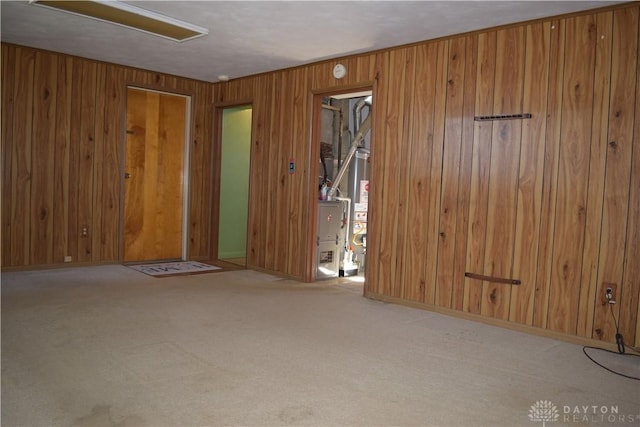 carpeted empty room featuring gas water heater and wooden walls