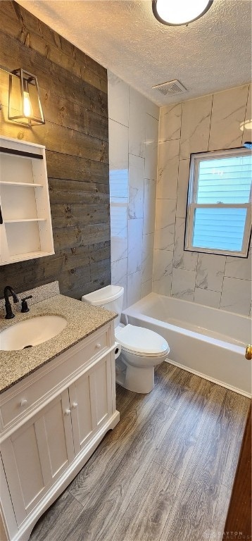 full bathroom featuring wood-type flooring, a textured ceiling, toilet, tiled shower / bath, and vanity