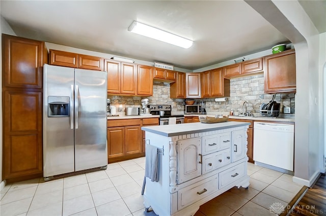 kitchen featuring a center island, backsplash, sink, appliances with stainless steel finishes, and light tile patterned flooring