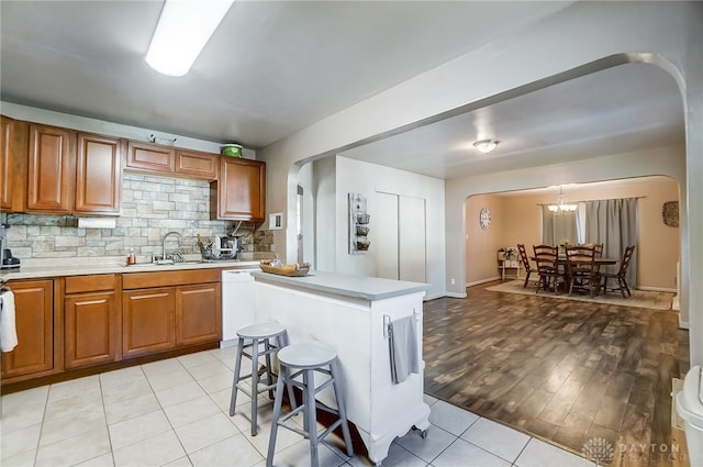 kitchen with white dishwasher, sink, light hardwood / wood-style flooring, a kitchen island, and a breakfast bar area