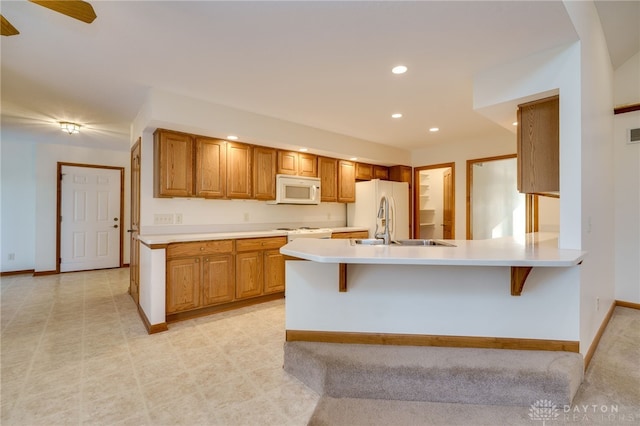 kitchen with white appliances, a kitchen breakfast bar, kitchen peninsula, and sink