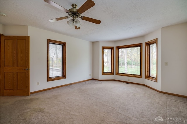 empty room featuring ceiling fan, light carpet, and a textured ceiling